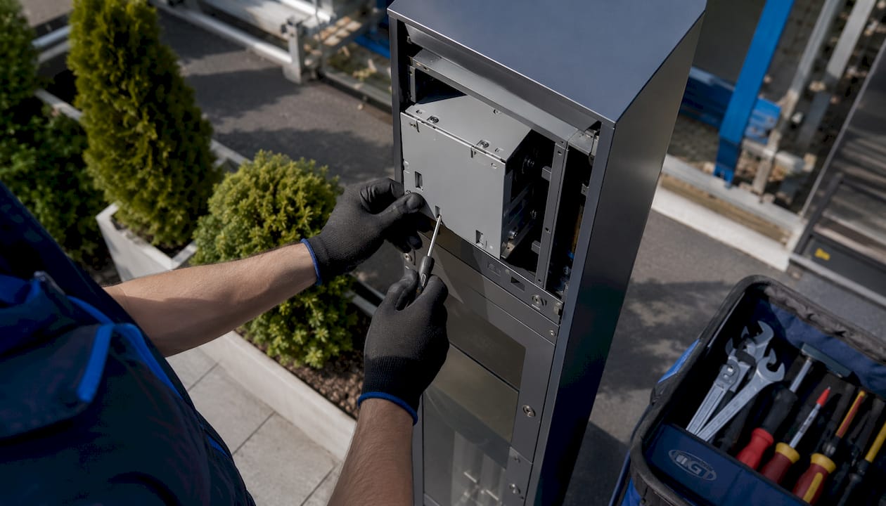 Dettaglio delle mani di un tecnico mentre installa un distributore di dispositivi di protezione individuale.
