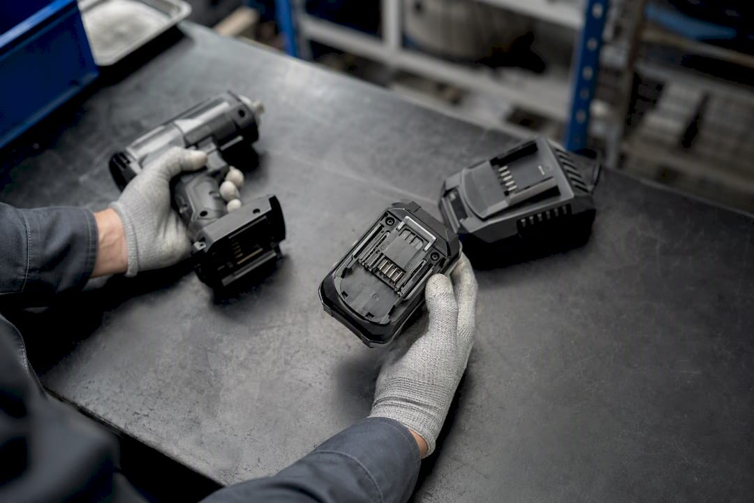 Mano guantata che rimuove la batteria di un utensile industriale