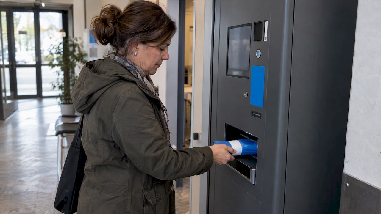 Una donna prende dei sacchetti da un distributore automatico
